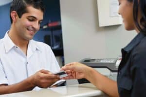 A male patient is handing over his credit card to the nurse at an office desk